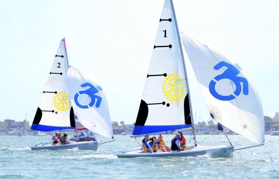 Two small sailboats with Rotary and accessibility symbols on their sails