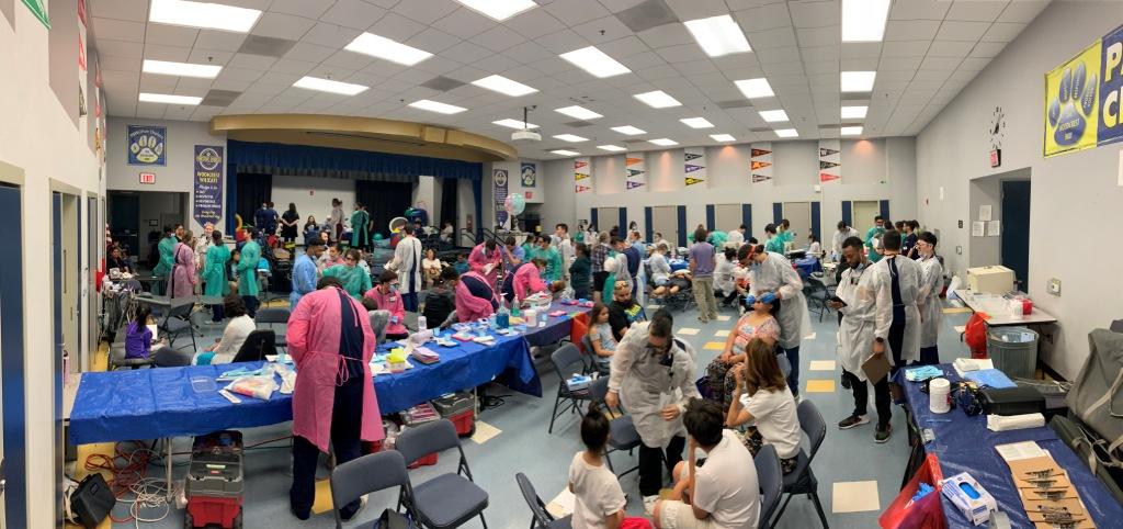 Volunteers and children at tables in a school multipurpose room