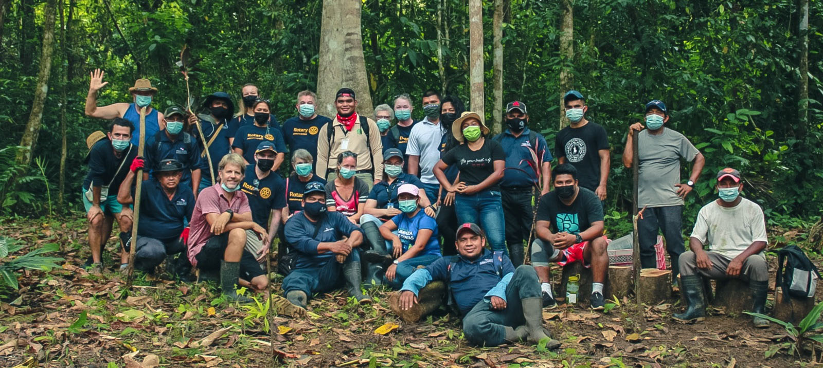 A large group of volunteers in work clothes gathered among trees at a project site